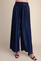 A person wearing dark navy wide-leg drawstring pants with black heeled sandals, shown from the waist down against a plain beige studio background.